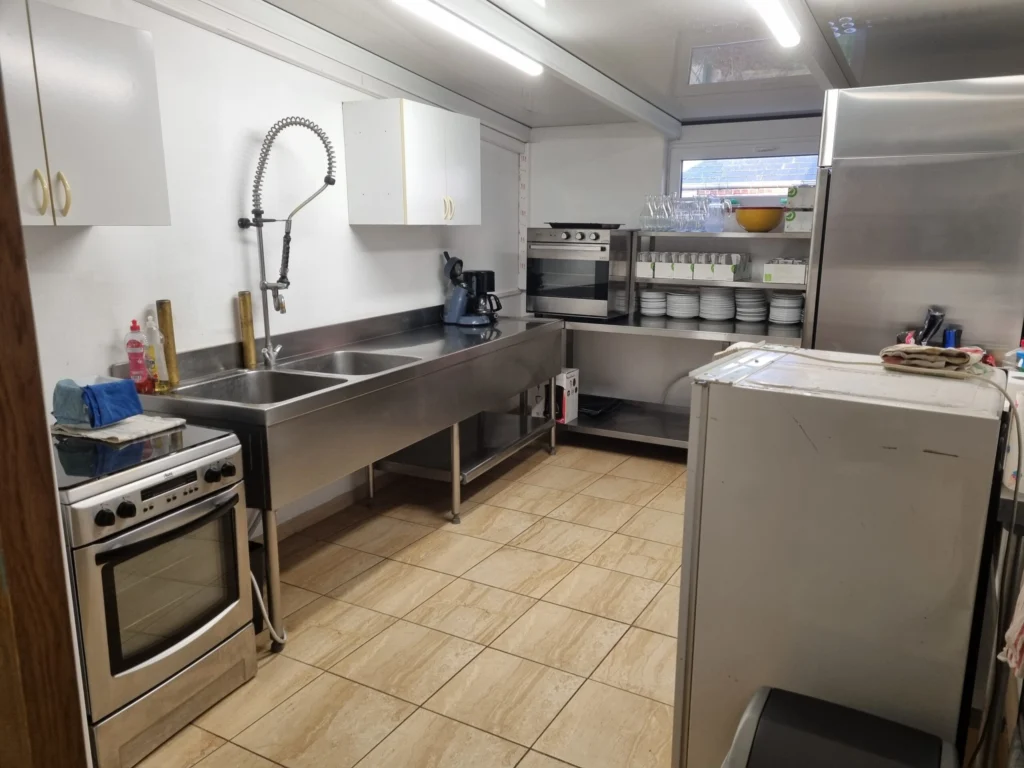 Cuisine de la salle des fêtes : plans de travail en inox, évier, four et réfrigérateur.