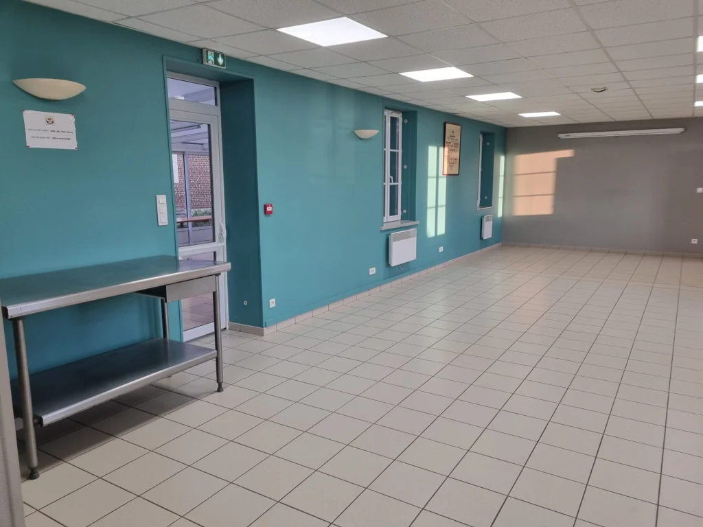 Grande salle des fêtes vue depuis l’entrée, avec une table de service en inox.